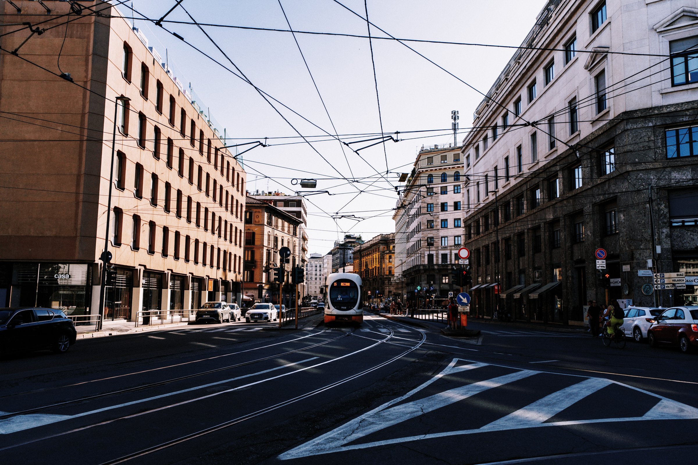 A tram crossing a city street in bright daylight, after