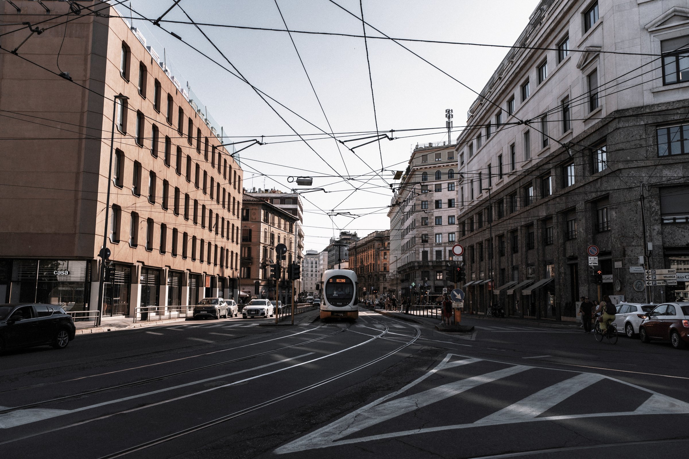 A tram crossing a city street in bright daylight, before