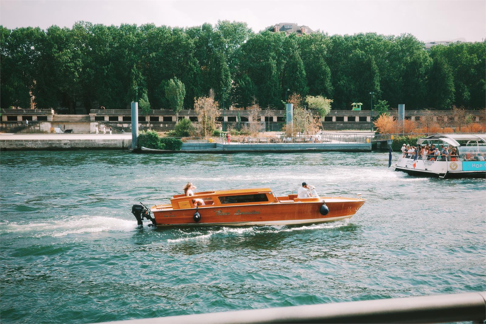 A wooden river boat passing a tree-lined bank in daylight, after