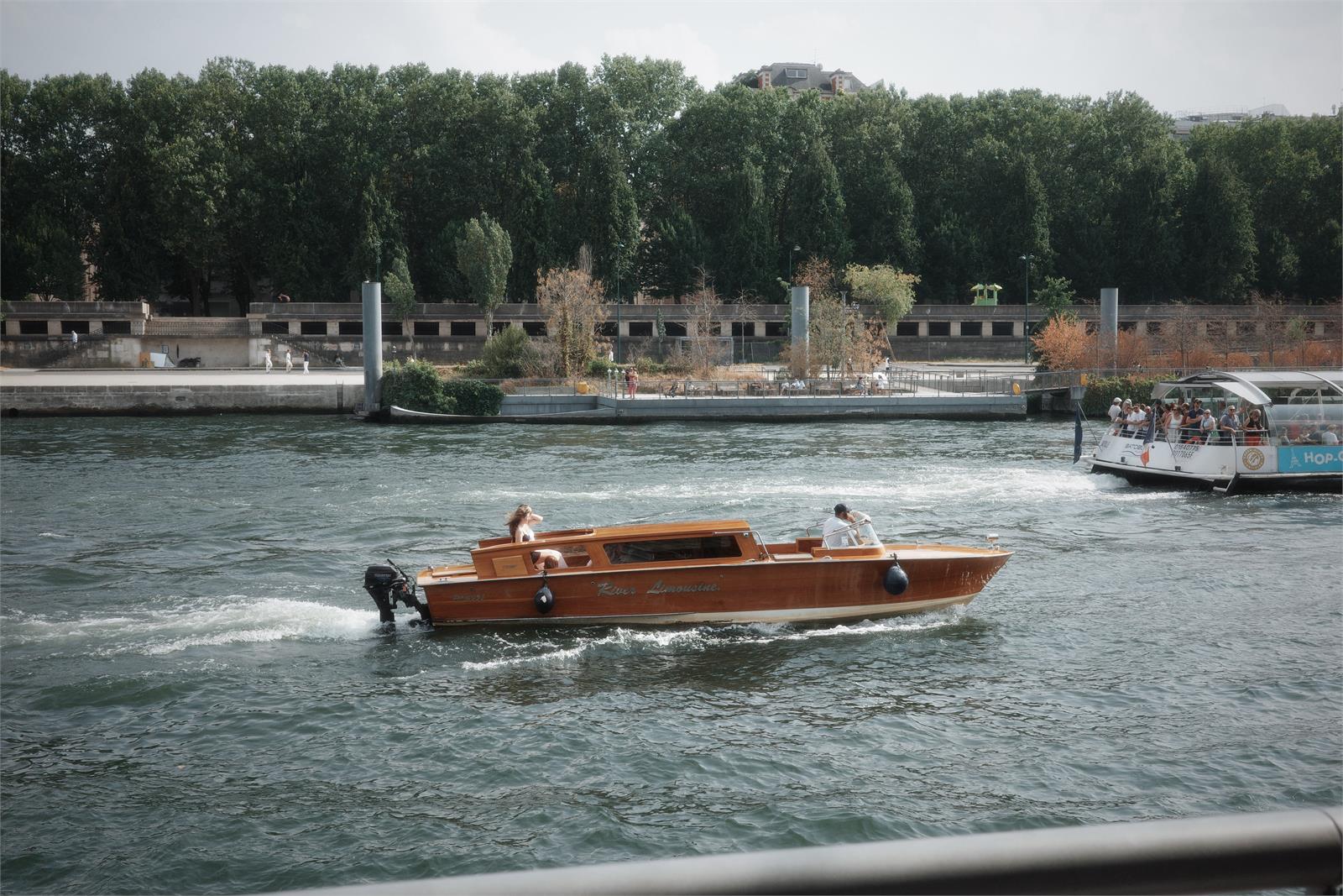 A wooden river boat passing a tree-lined bank in daylight, before