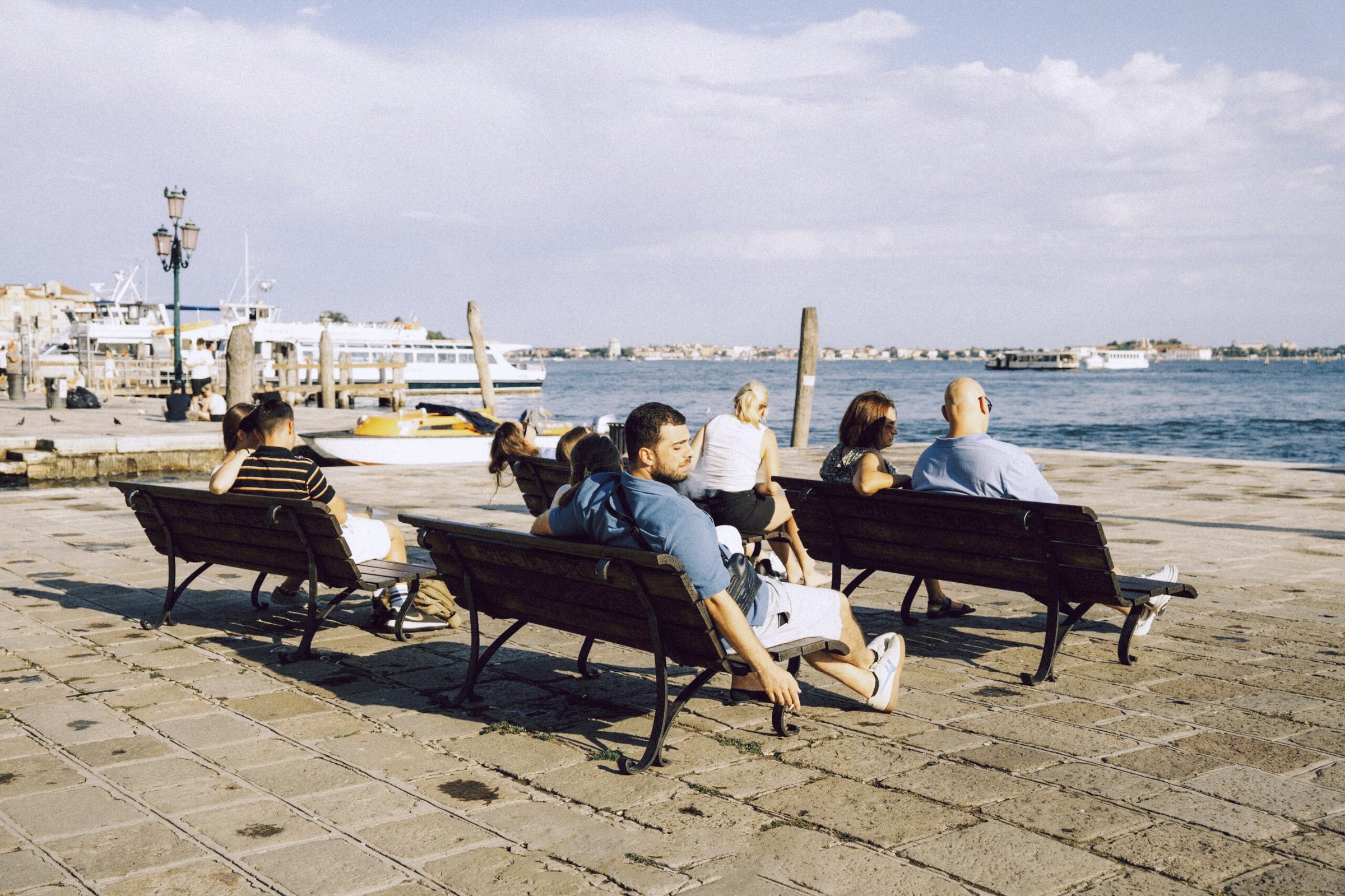 People sitting on waterfront benches beside a harbor in daylight, after