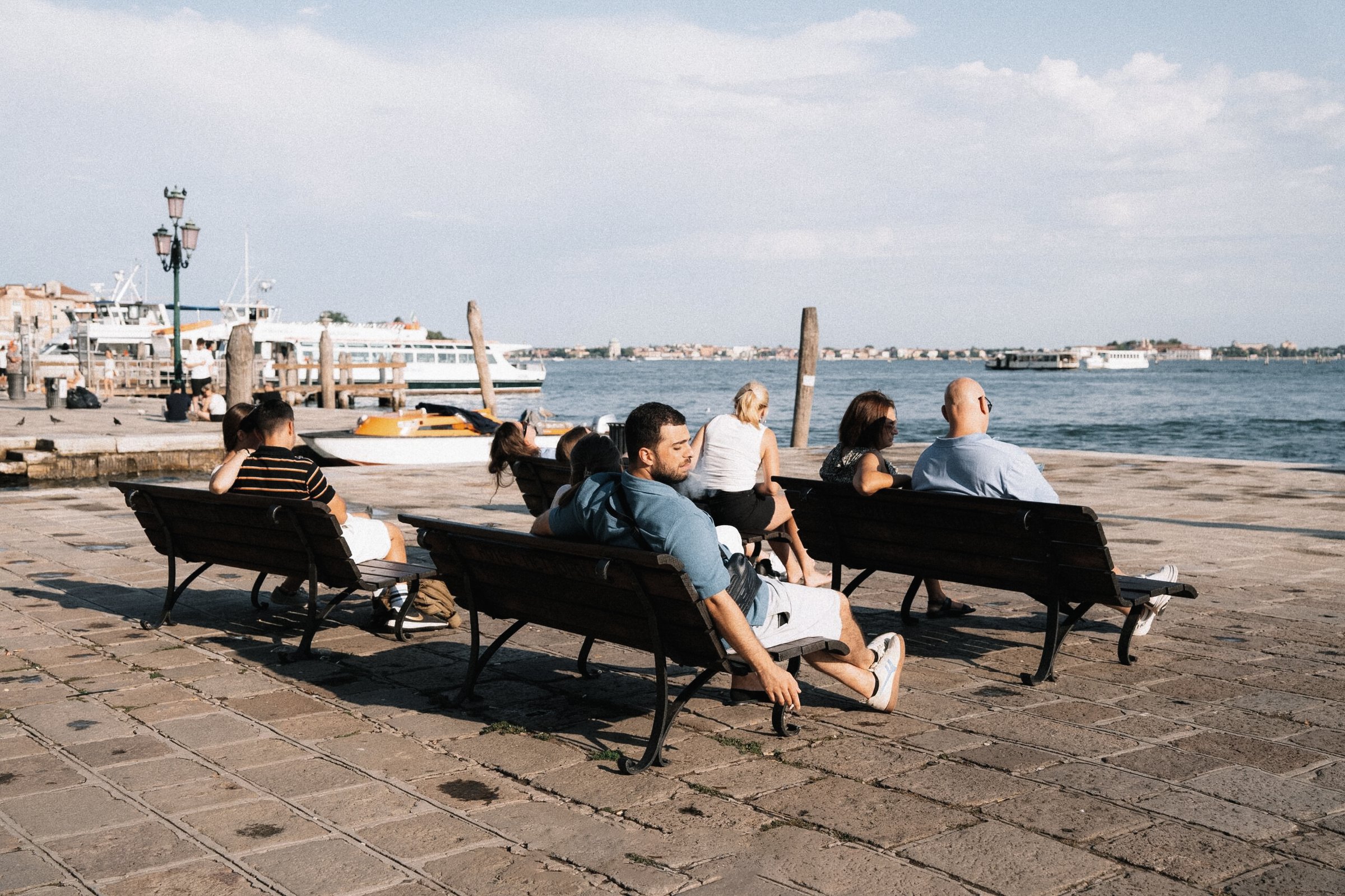 People sitting on waterfront benches beside a harbor in daylight, before