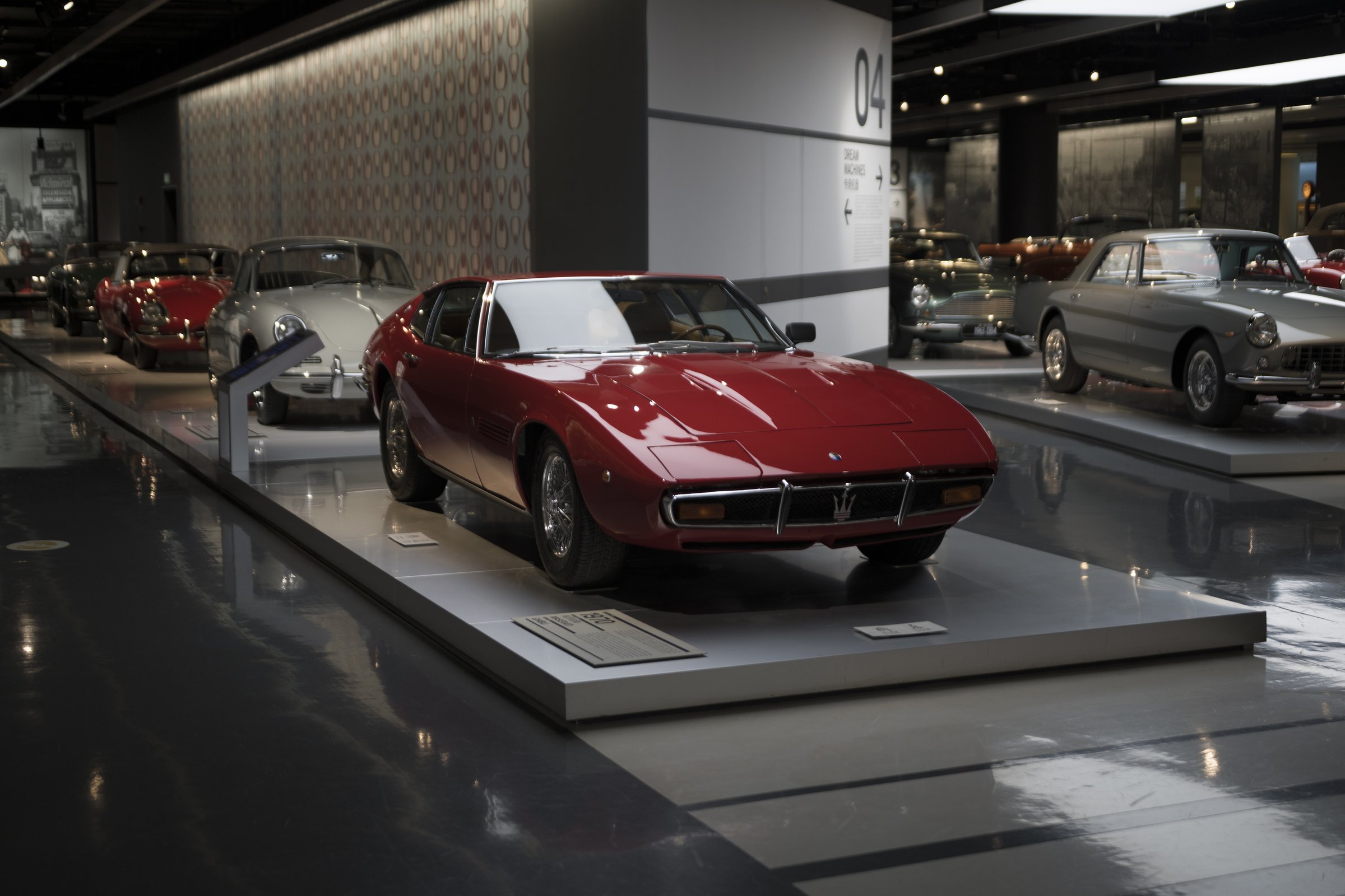 A red classic Maserati displayed in an indoor car museum, before