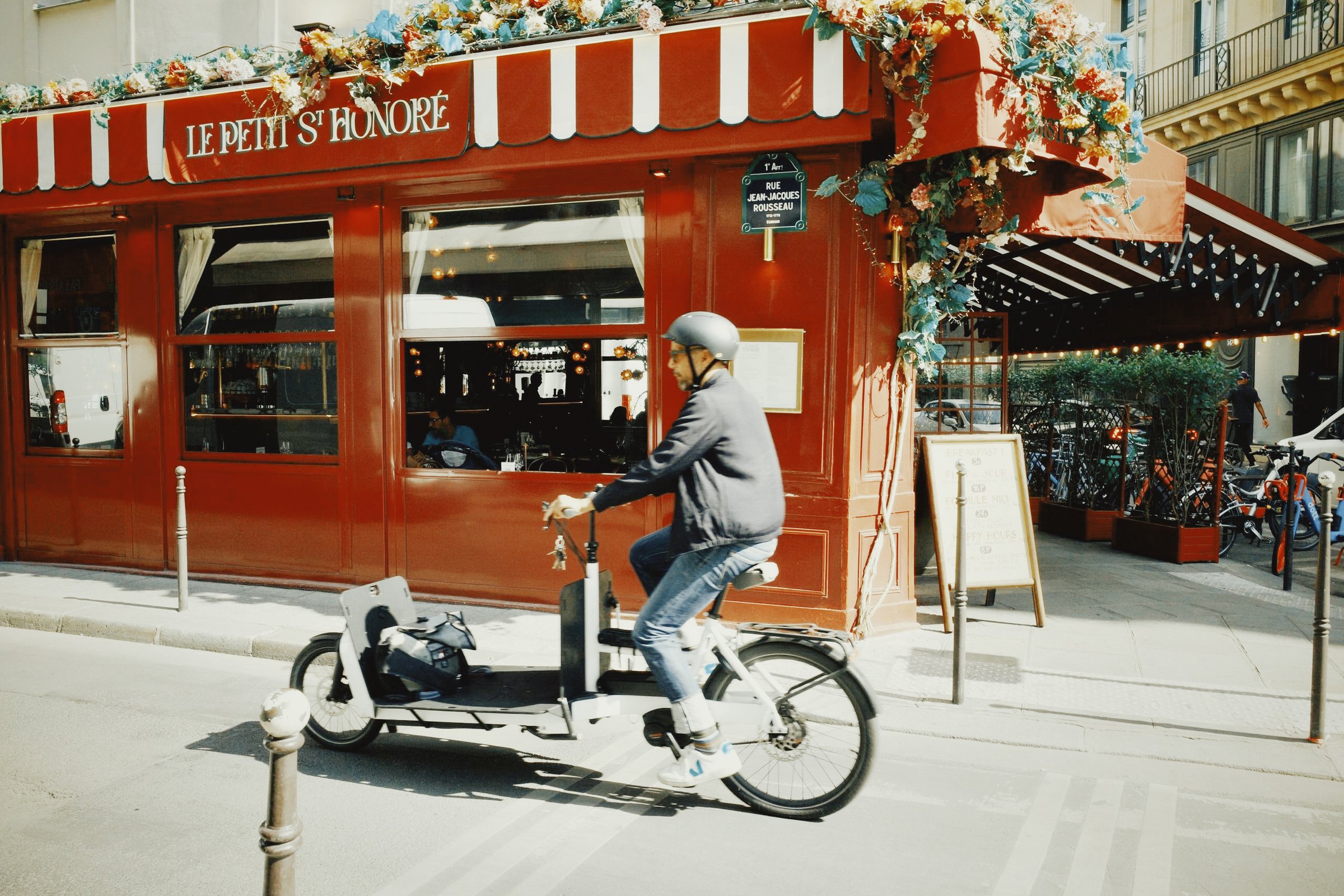 A cyclist passing a red Paris cafe in daylight, after