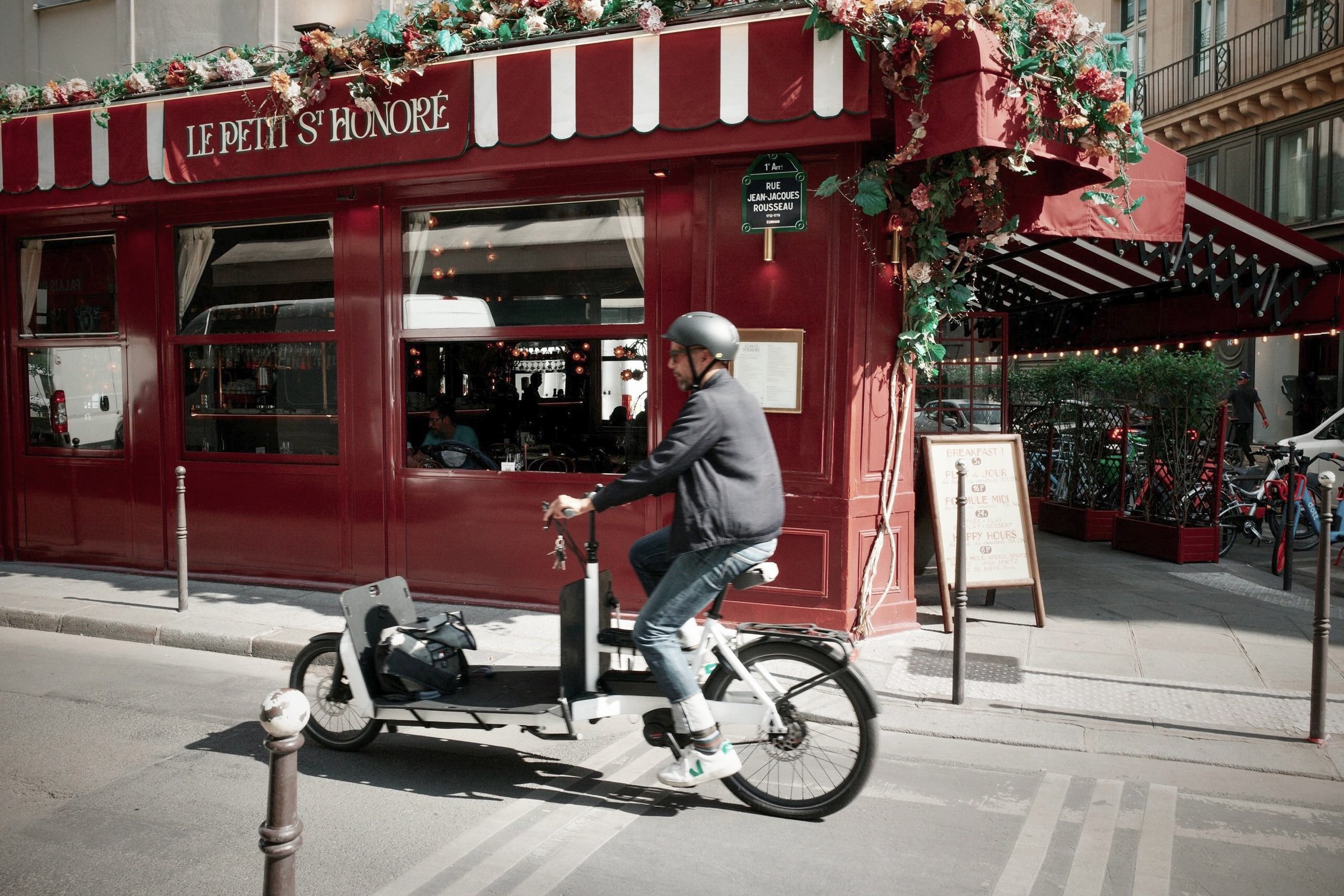 A cyclist passing a red Paris cafe in daylight, before
