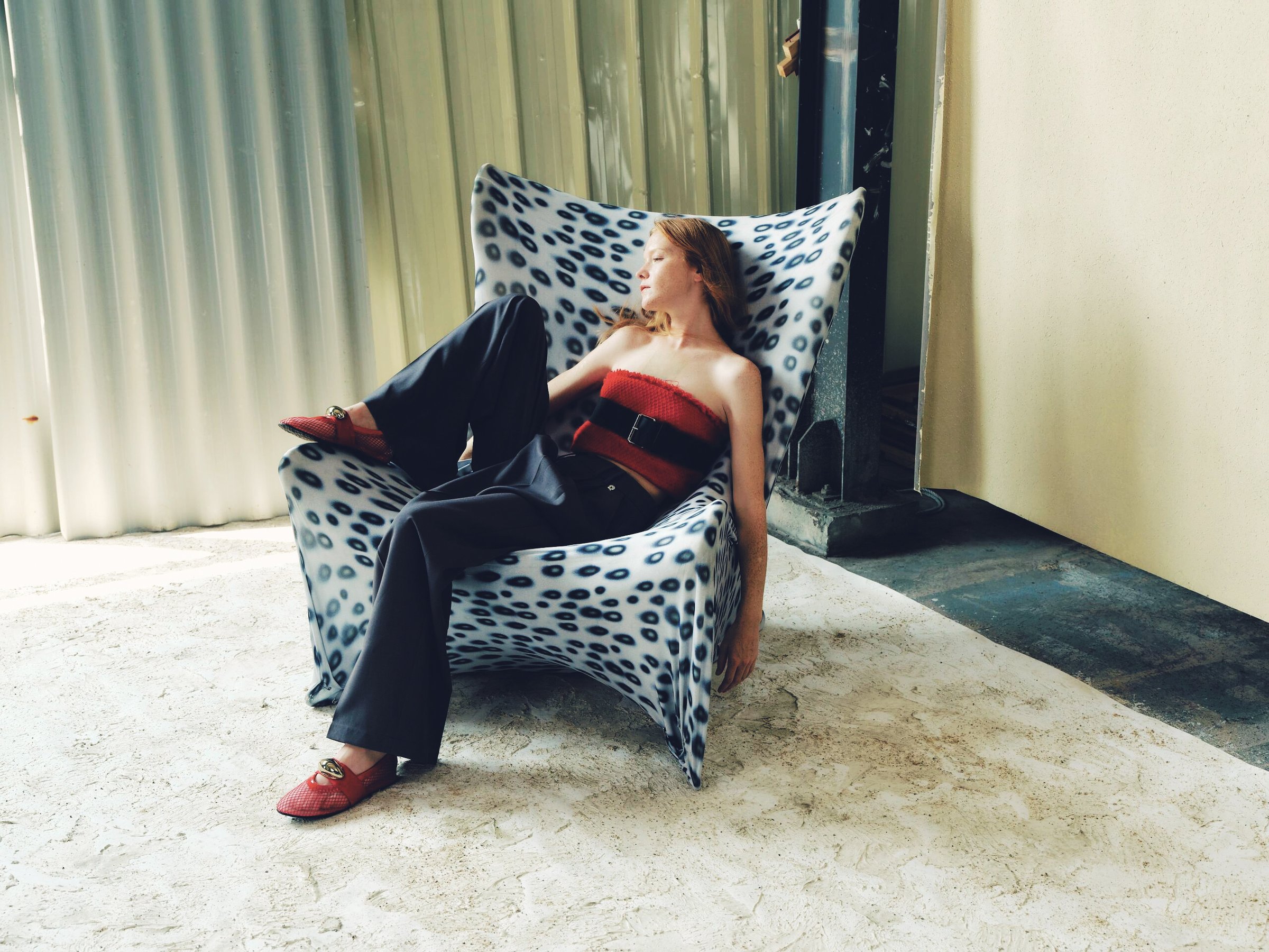 A model in red and black reclining on a polka-dot armchair, after