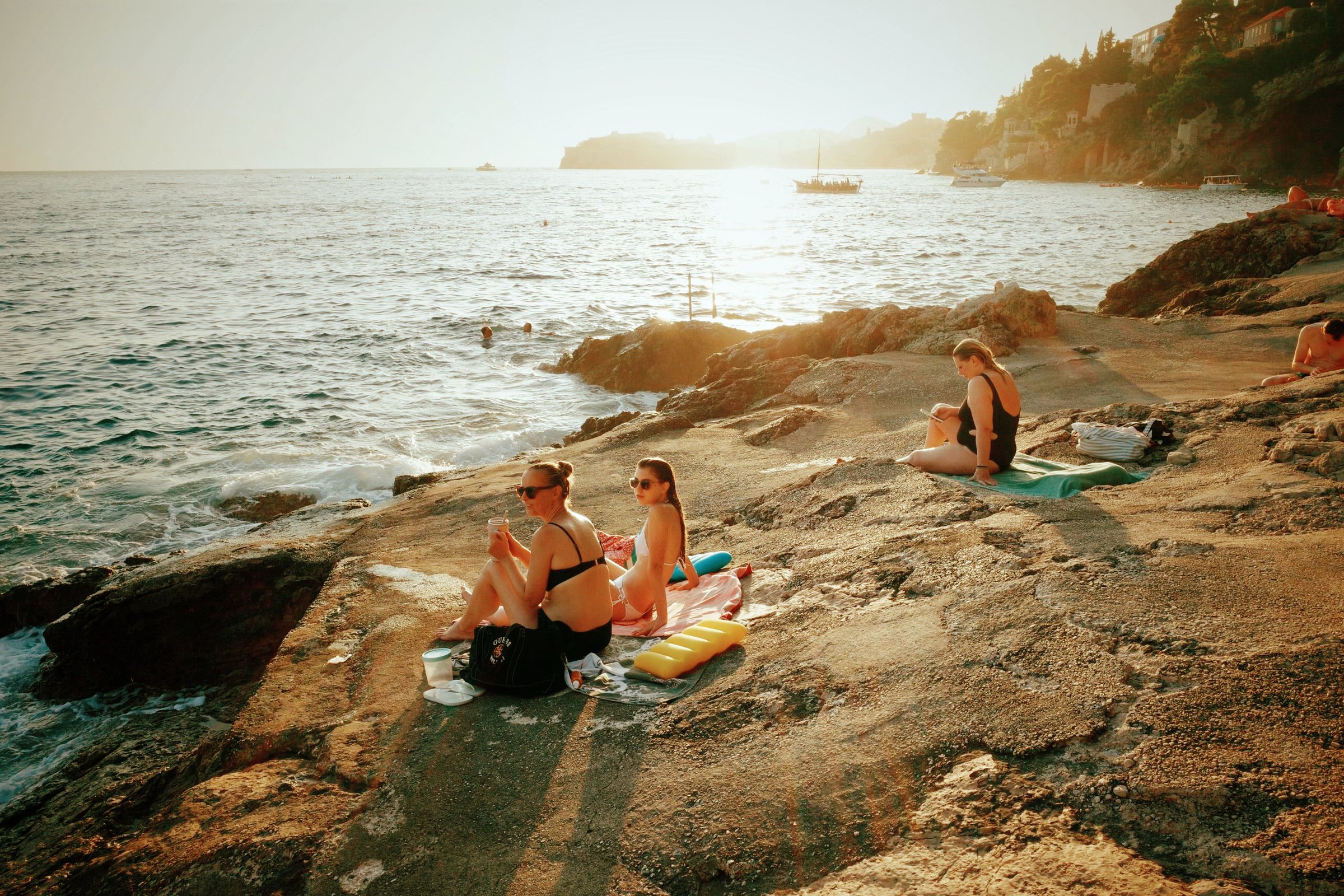 People sunbathing on a rocky coastline in bright daylight, after
