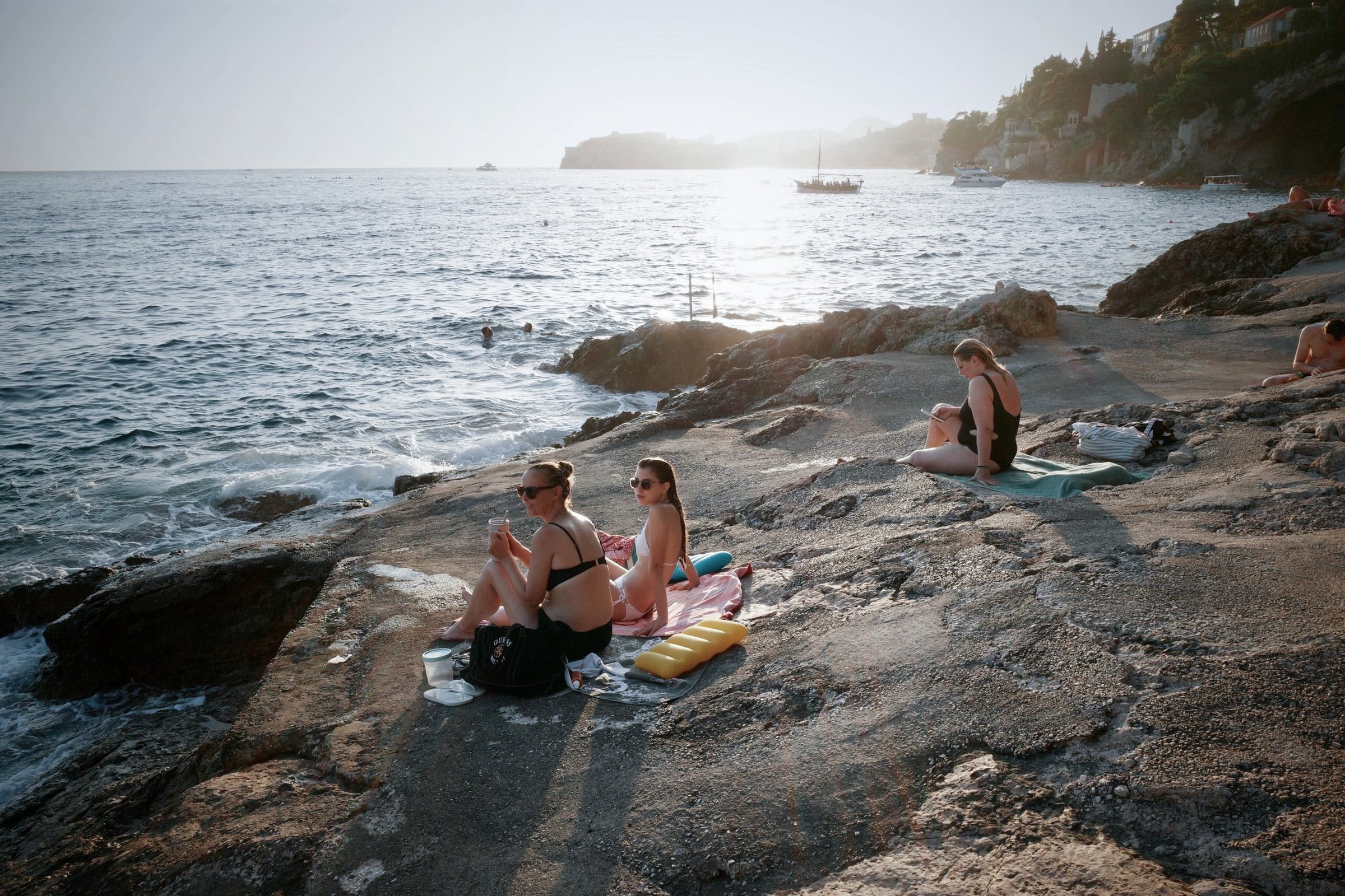 People sunbathing on a rocky coastline in bright daylight, before